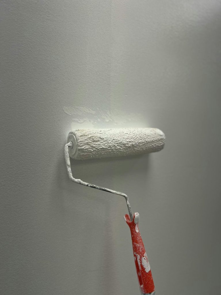 A paint roller applying white paint on a smooth wall. DIY home renovation concept.